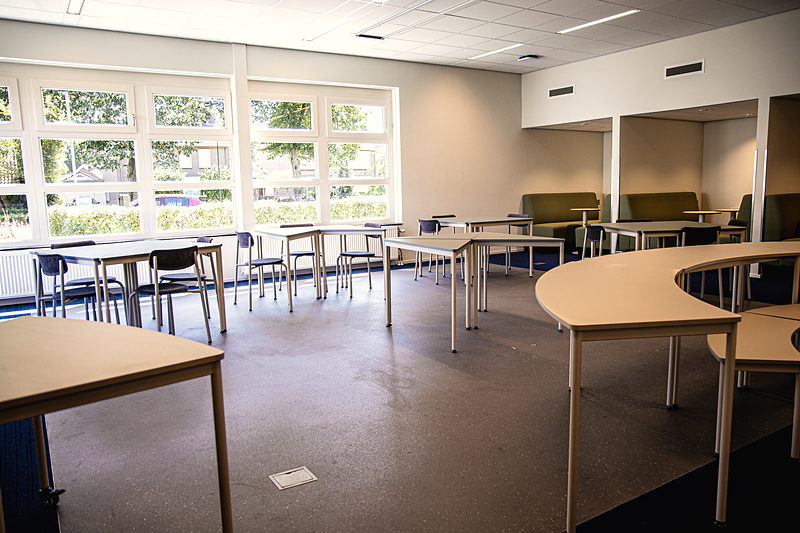 Werkplekken bij het raam en groene zitnissen in een lokaal van SAM College
